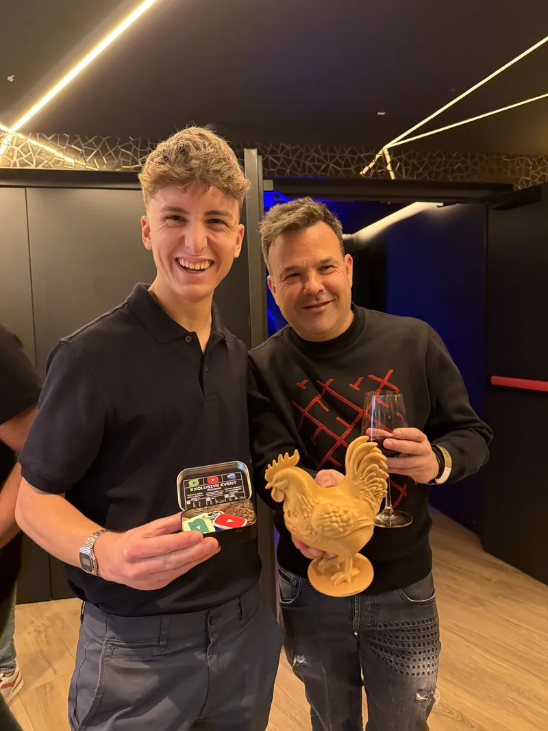 Uriel, con polo negro, sujeta una lata de NFC abierta junto a José Elías, que sostiene una figura de un gallo impresa en 3D.