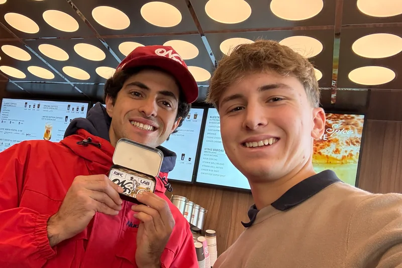 Uriel y un miembro del equipo de Nude Project sonriendo en la barra de su cafetería, sujetando una lata metálica de NFC.