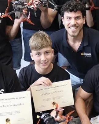 Uriel de chaval, con camiseta negra, sujeta su diploma en una foto de grupo de deDrones Academy, con drones FPV en alto detrás.
